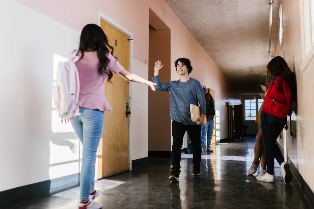 students-standing-on-a-hallway-8419249 Teens greeting each other happily in a school hallway with natural light.