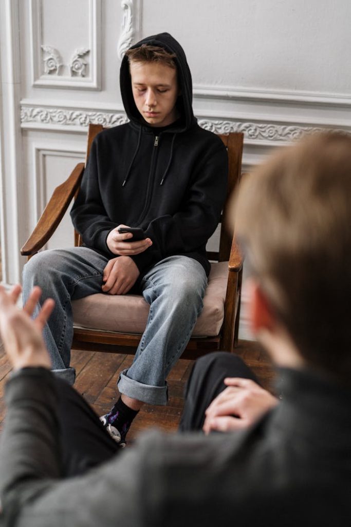woman-in-black-hijab-and-blue-denim-jeans-sitting-on-brown-wooden-armchair-4100656 Teen sitting in therapy session with counselor in a modern office setting.